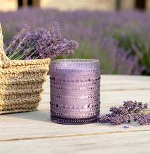 Load image into Gallery viewer, Vanilla and Lavender scented candle in purple hobnail glass jar on a wooden surface with lavender field in background.