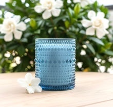 Load image into Gallery viewer, Jasmine and Gardenia scented candle on a wooden surface with white flowers and green foliage in the background.