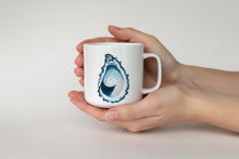 Load image into Gallery viewer, Person holding a mug with an oyster shell design on a light gray background