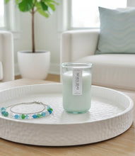 Load image into Gallery viewer, Seven Seas natural wax candle on a white tray with a plant and a white couch in the background.