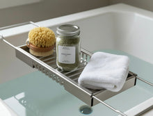Load image into Gallery viewer, Ocean Purity bath soak in a glass jar on a bathtub tray with a natural sponge and folded white towel over a tub filled with pale blue water.