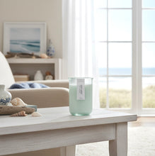 Load image into Gallery viewer, Sea Mist candle on a coffee table with a coastal view through large windows