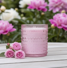 Load image into Gallery viewer, Rose and Peony scented candle displayed in a garden with pink roses and peonies in the background.