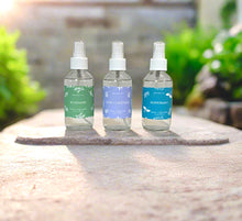 Load image into Gallery viewer, Garden collection room sprays-Rosemary, Sage & Lavender, and Peppermint on a stone surface with a garden background.