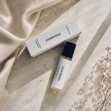 Load image into Gallery viewer, SAHARA ROSE perfume oil from the Maison de Parfum collection with matching box, styled on a textured beige stone surface next to draped cream satin fabric and delicate dried flowers.
