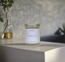 Load image into Gallery viewer, Tonka + Oud candle styled on a concrete surface with urban textures and minimal decor