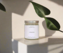 Load image into Gallery viewer, Havana candle styled on a minimal space, green leaf in the background with a shadow falling over