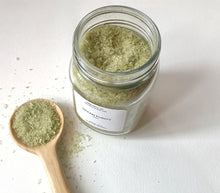 Load image into Gallery viewer, Open jar of Ocean Purity bath soak with a wooden scoop filled with green bath salts on a clean white background.
