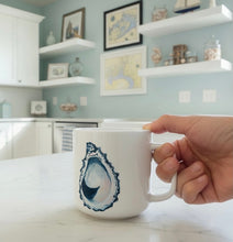 Load image into Gallery viewer, Hand holding a mug with an oyster design in a kitchen setting

