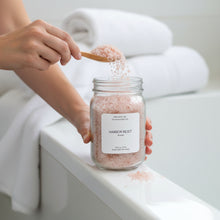 Load image into Gallery viewer, Handing holding Harbor Reset bath soak while scooping salts above a white bathtub. 

