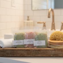 Load image into Gallery viewer, Three bath salt sample packages on a wooden tray with a bathroom setting in the background.
