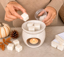Load image into Gallery viewer, Soy wax melt cubes being placed in a ceramic wax warmer with a lit tealight for a cozy fall home fragrance.
