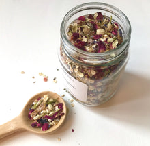Load image into Gallery viewer, Open jar of Root Ritual bath tea with a wooden scoop filled with dried botanicals on a white background.
