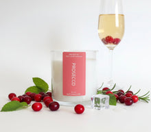 Load image into Gallery viewer, Clear tumbler jar candle, styled with a sparkling champagne glass and cranberries in the background, conveying a bubbly and fruity prosecco scent.
