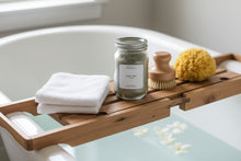 Load image into Gallery viewer, Quiet Tide bath soak in a glass jar on a bathtub tray with a natural sponge, dry brush and folded white towel over a tub filled with pale blue water.
