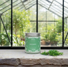 Load image into Gallery viewer, Earthy rosemary candle on a stone surface with greenhouse background.
